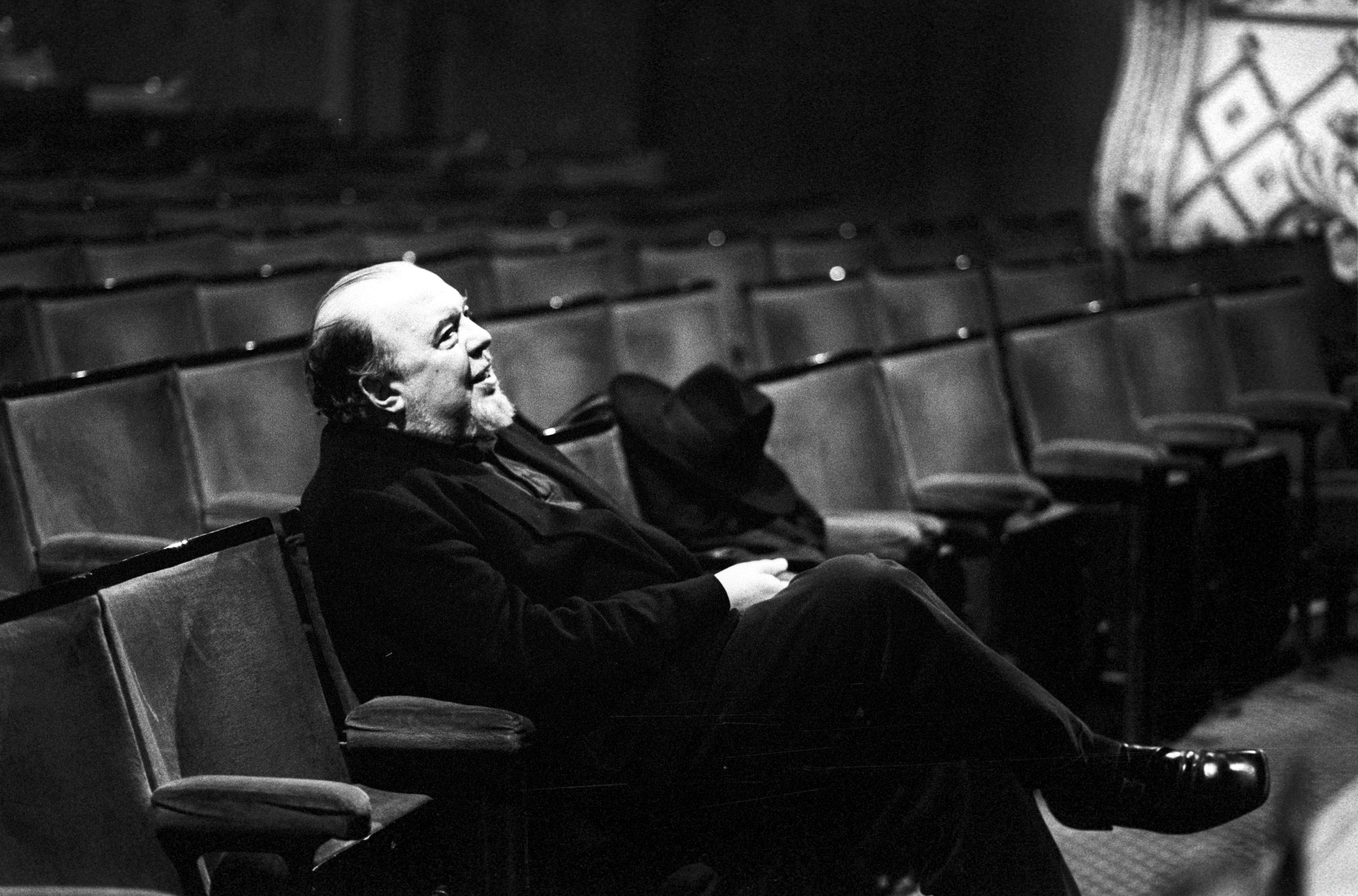 A black and white photograph of Sir Peter Hall seated at the front of The Old Vic stalls
