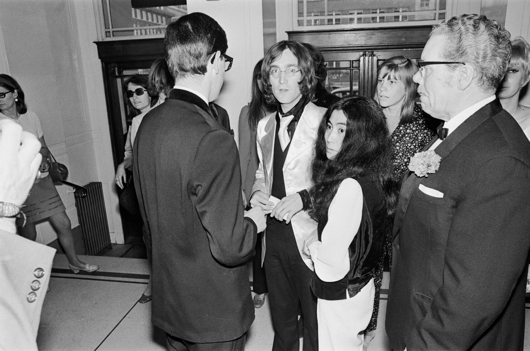 John Lennon and Yoko Ono stand in a crowd of people outside The Old Vic