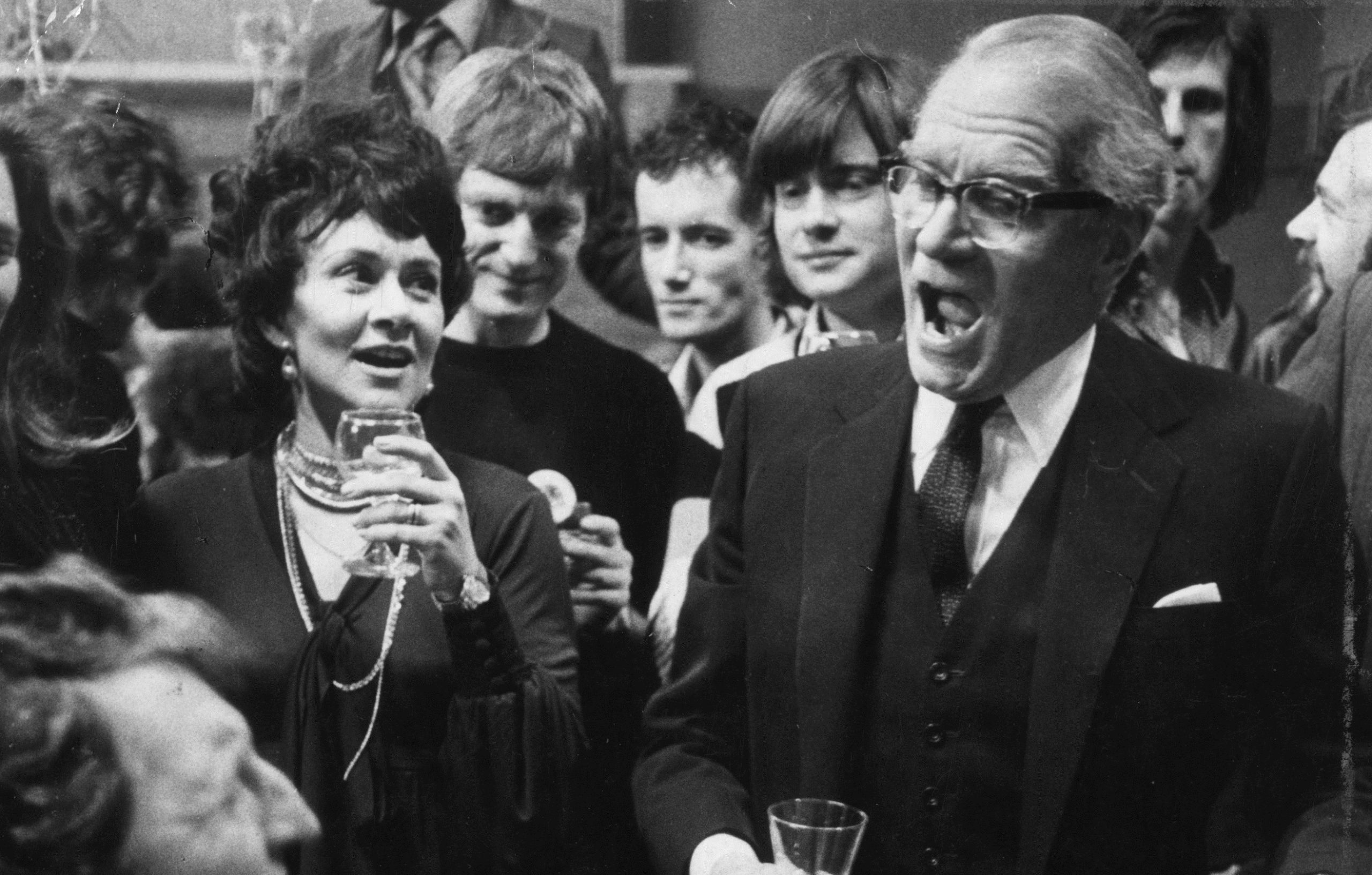 Laurence Olivier stands next to Joan Plowright in the rehearsal room - he sings as a crowd listen