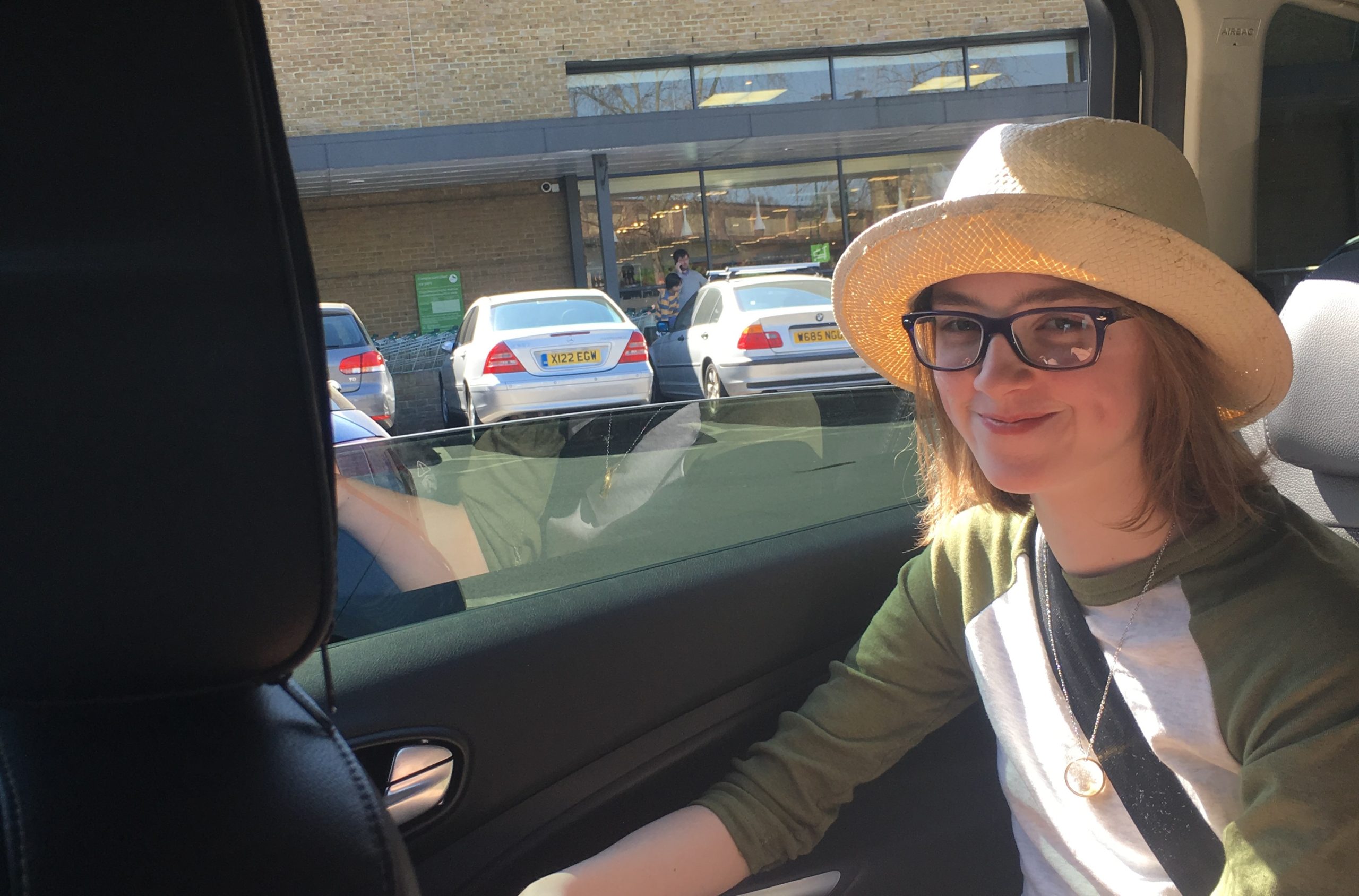 Bella sits in a car wearing a hat and smiling at the camera