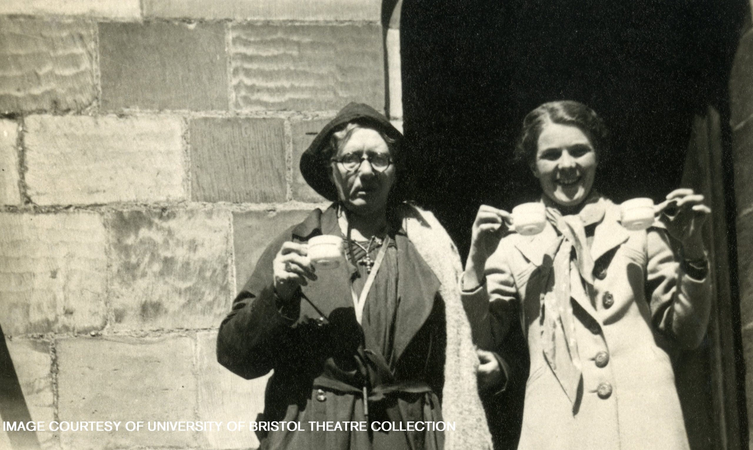 Lilian Baylis stands outside next to a woman, both holding teacups