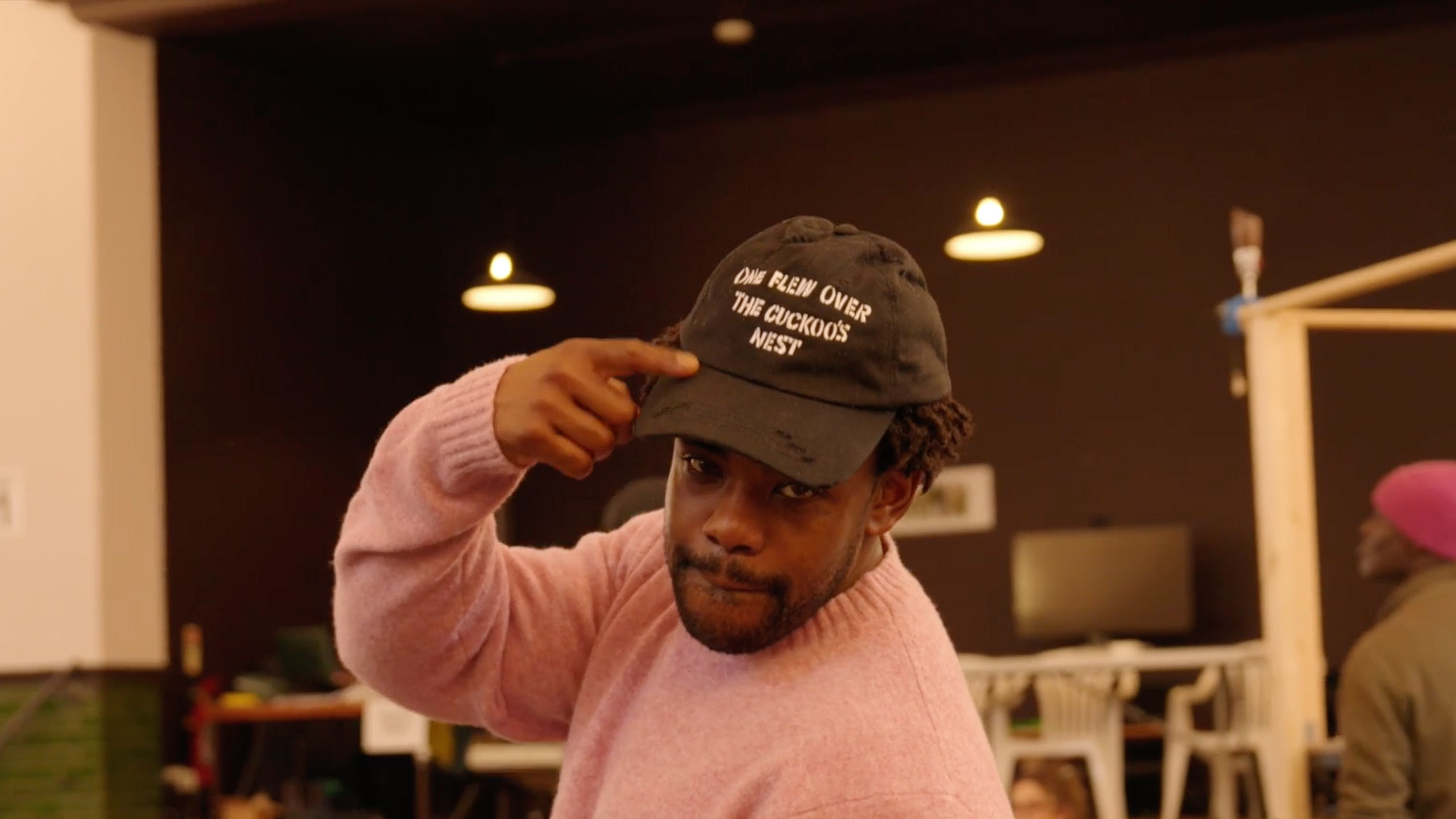 Actor Shaquille Jack points to a black cap he's wearing which says 'One Flew Over the Cuckoo's Nest' on it.