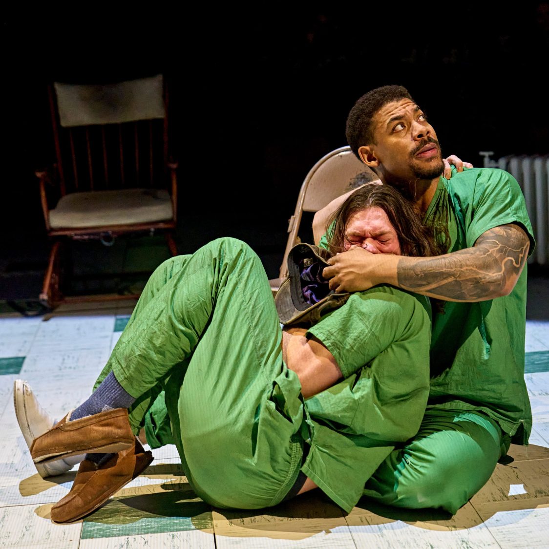 Actor Aaron Pierre cradles actor Arthur Boan in his arms. Aaron muffles Arthur's cries with his hand and looks up at a presence above.