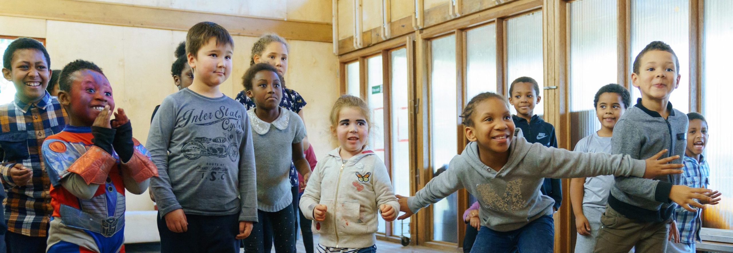 A group of primary school-aged children are dressed in their own clothes, smiling and posing in freeze-frame positions.