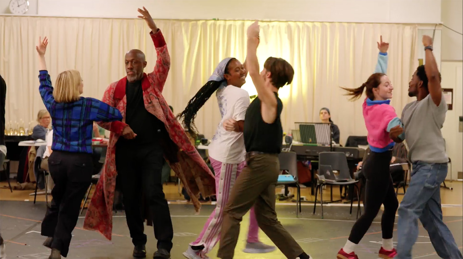 The cast of A Christmas Carol dance a jig together, stood in a line in a rehearsal room
