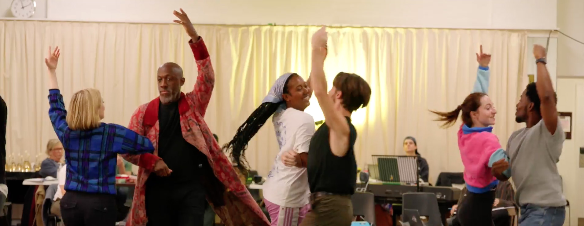 The cast of A Christmas Carol dance a jig together, stood in a line in a rehearsal room